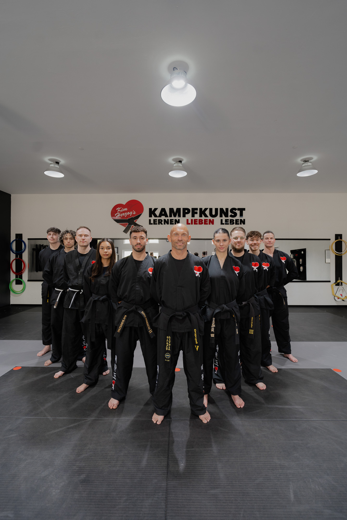 Das Team von KAMPFKUNST HERZ® in schwarzen Anzügen im Dojo